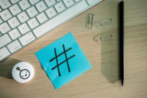 top view of a keyboard paper clips pencil and a sticky note with a hashtag on it lying on a desk
