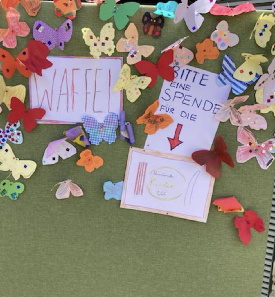 Eine Stellwand mit vielen bunten selbst gebastelten Schmetterlingen. Ein Schild mit der Aufschrift "Waffel". Daneben das Schild "Bitte eine SPende für die Hannöversche Kinder Tafel"